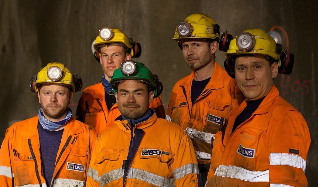 5 arbeidere med orange uniform, hjelm med lys og hørselvern