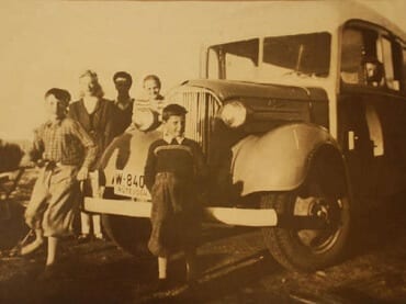 Gammelt bilde av personer som står ved siden av en gammel lastebil